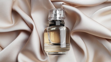 Luxury bottle of perfume on beige silk, top view