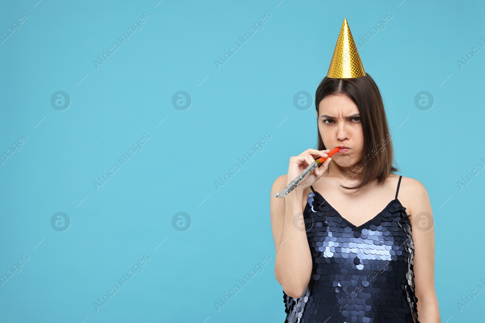 Photo of Sad young woman in party hat with blower on light blue background