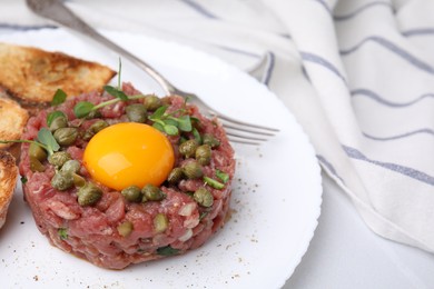 Photo of Tasty beef steak tartare served with yolk, capers and toasted bread on white table, closeup
