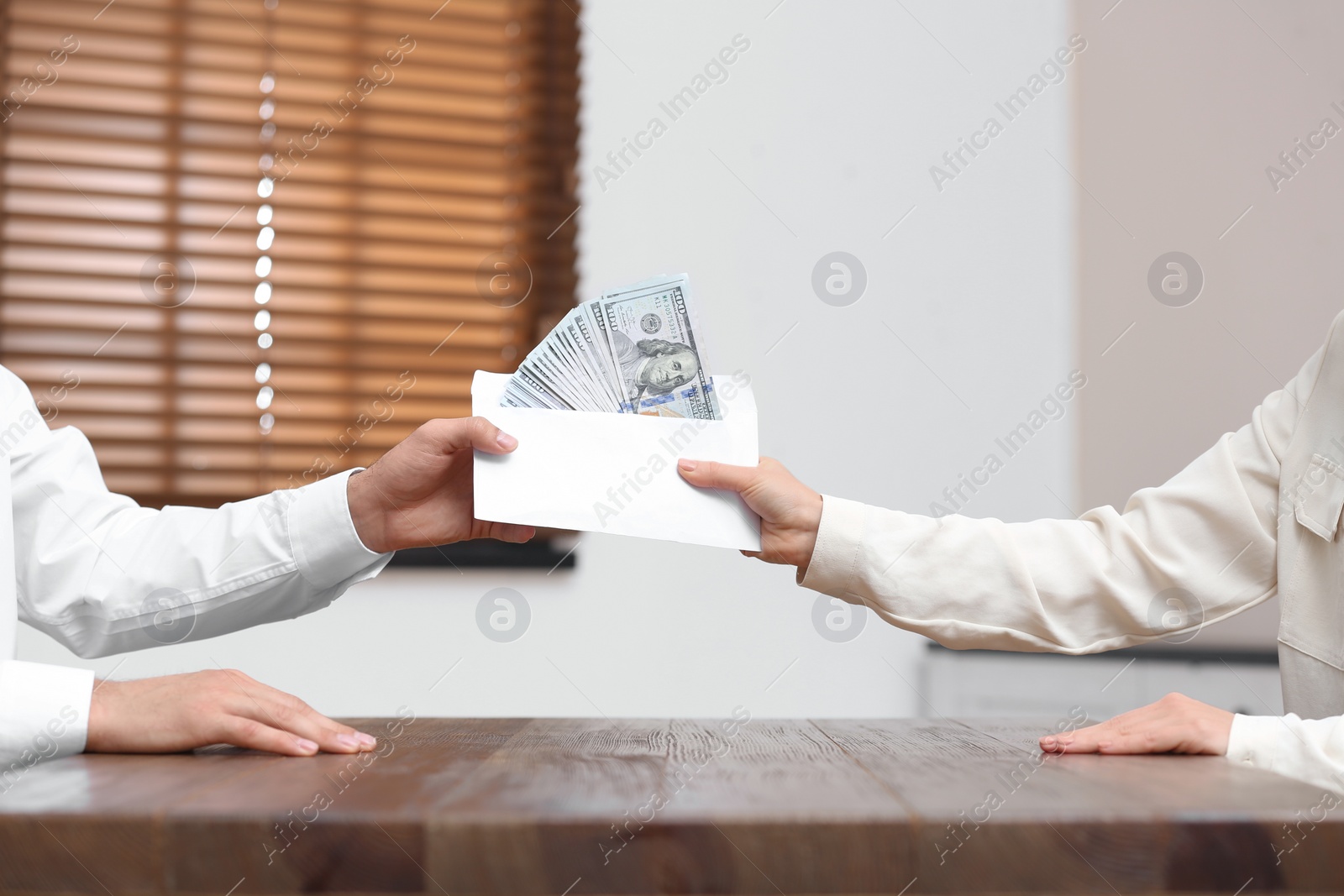 Photo of Woman giving bribe money to man at table indoors, closeup