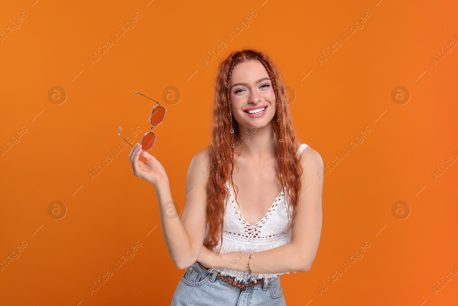 Photo of Stylish young hippie woman with sunglasses on orange background