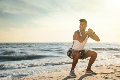 Photo of Sporty man doing exercise on sandy beach at sunset