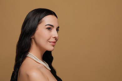 Photo of Young woman wearing elegant pearl necklace on brown background, space for text