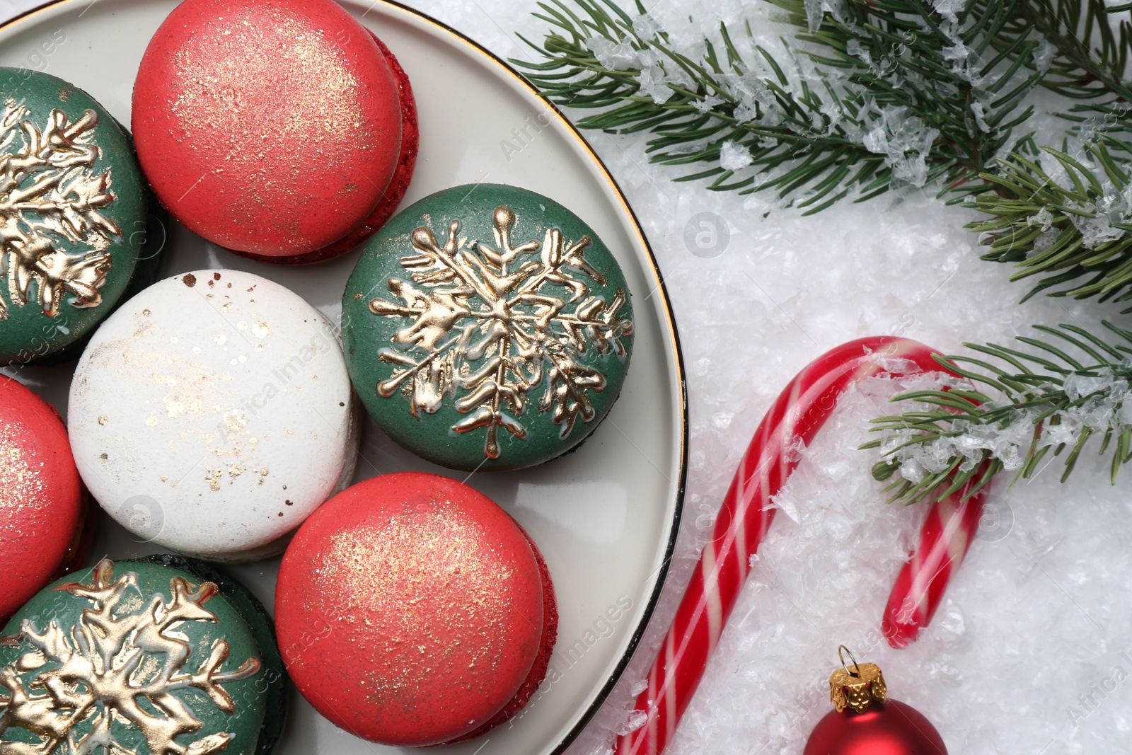 Photo of Beautifully decorated Christmas macarons, candy cane and festive decor on snow, flat lay