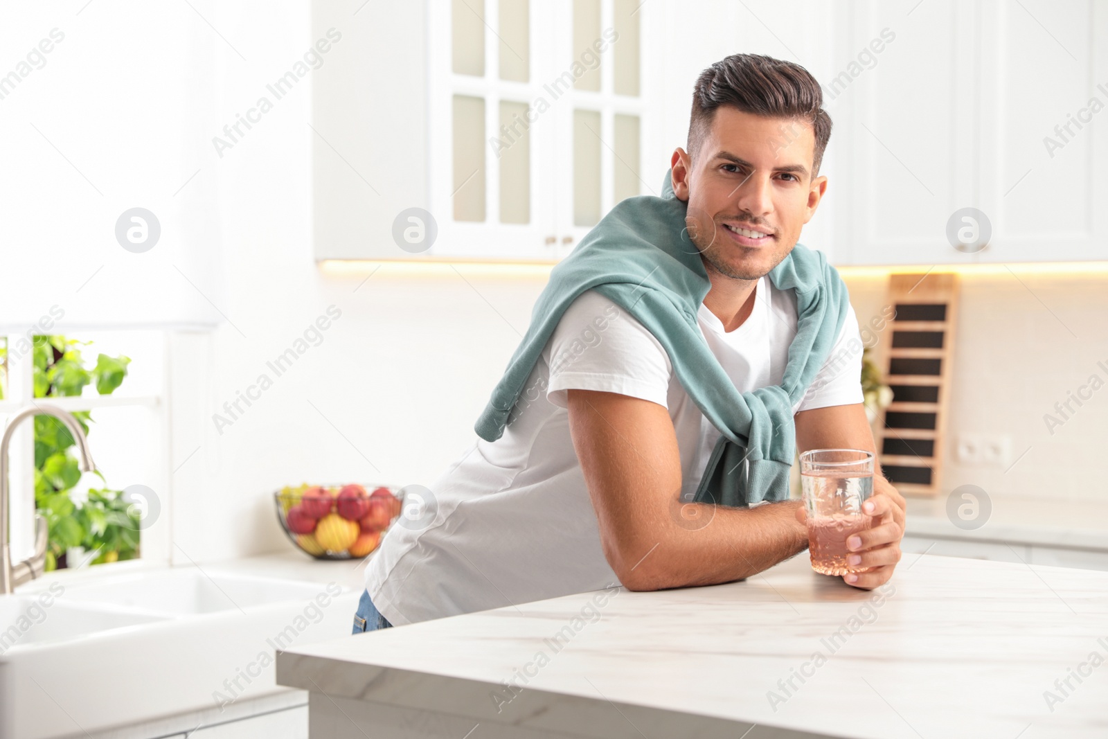 Photo of Man holding glass of pure water at table in kitchen