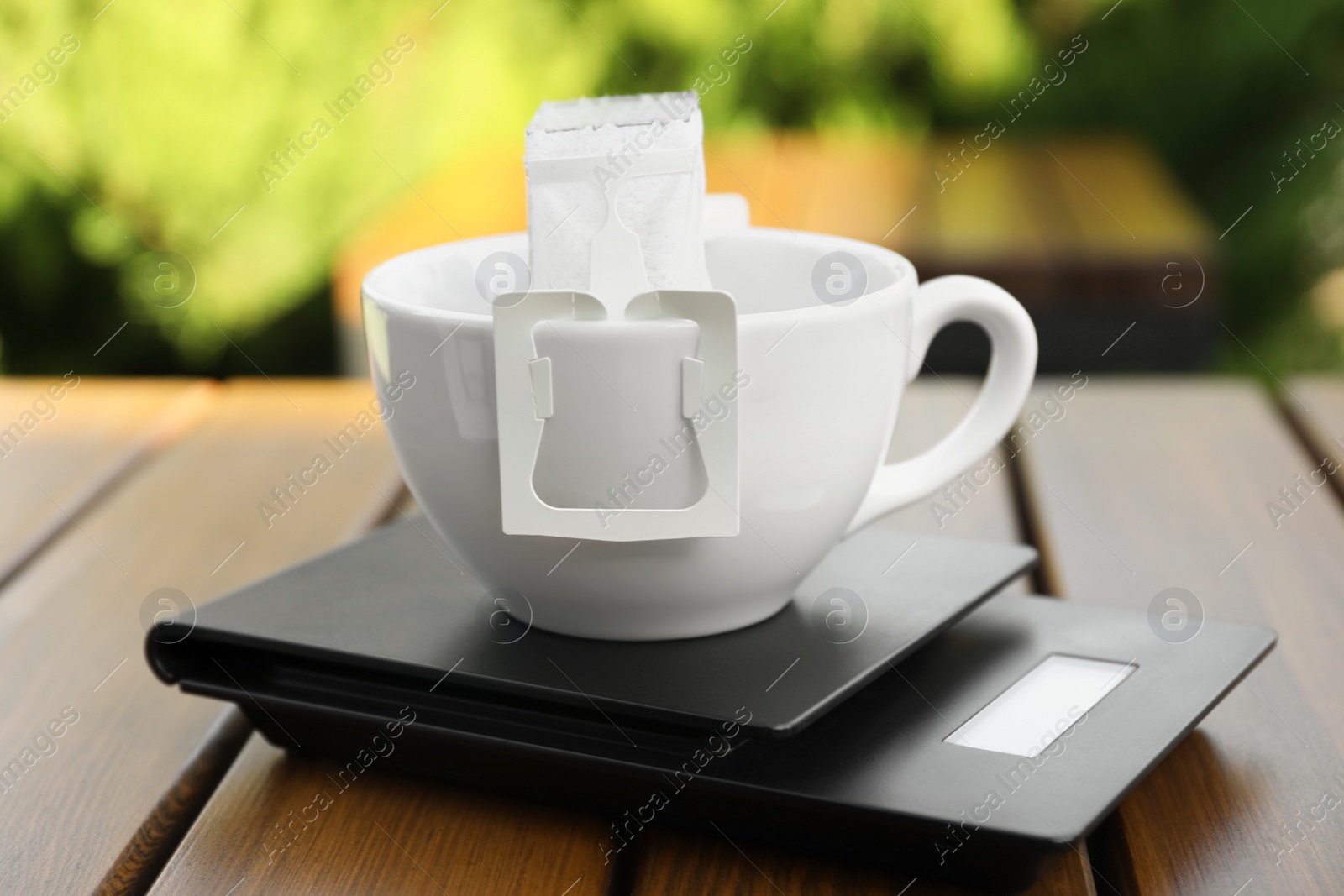 Photo of Cup with drip coffee bag and kitchen scales on wooden table, closeup