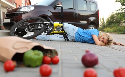 Photo of Woman fallen from bicycle after car accident and scattered vegetables on street