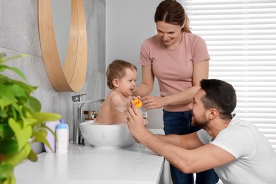 Photo of Father and mother washing their little baby in sink at home