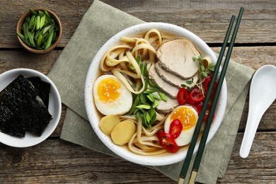 Photo of Delicious ramen in bowl served on wooden table, flat lay. Noodle soup