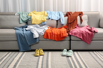 Photo of Shoes near sofa with different clothes indoors