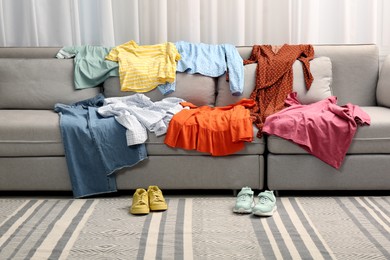 Shoes near sofa with different clothes indoors