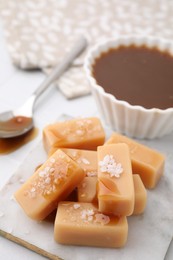 Photo of Delicious candies with sea salt and caramel sauce on white tiled table, closeup