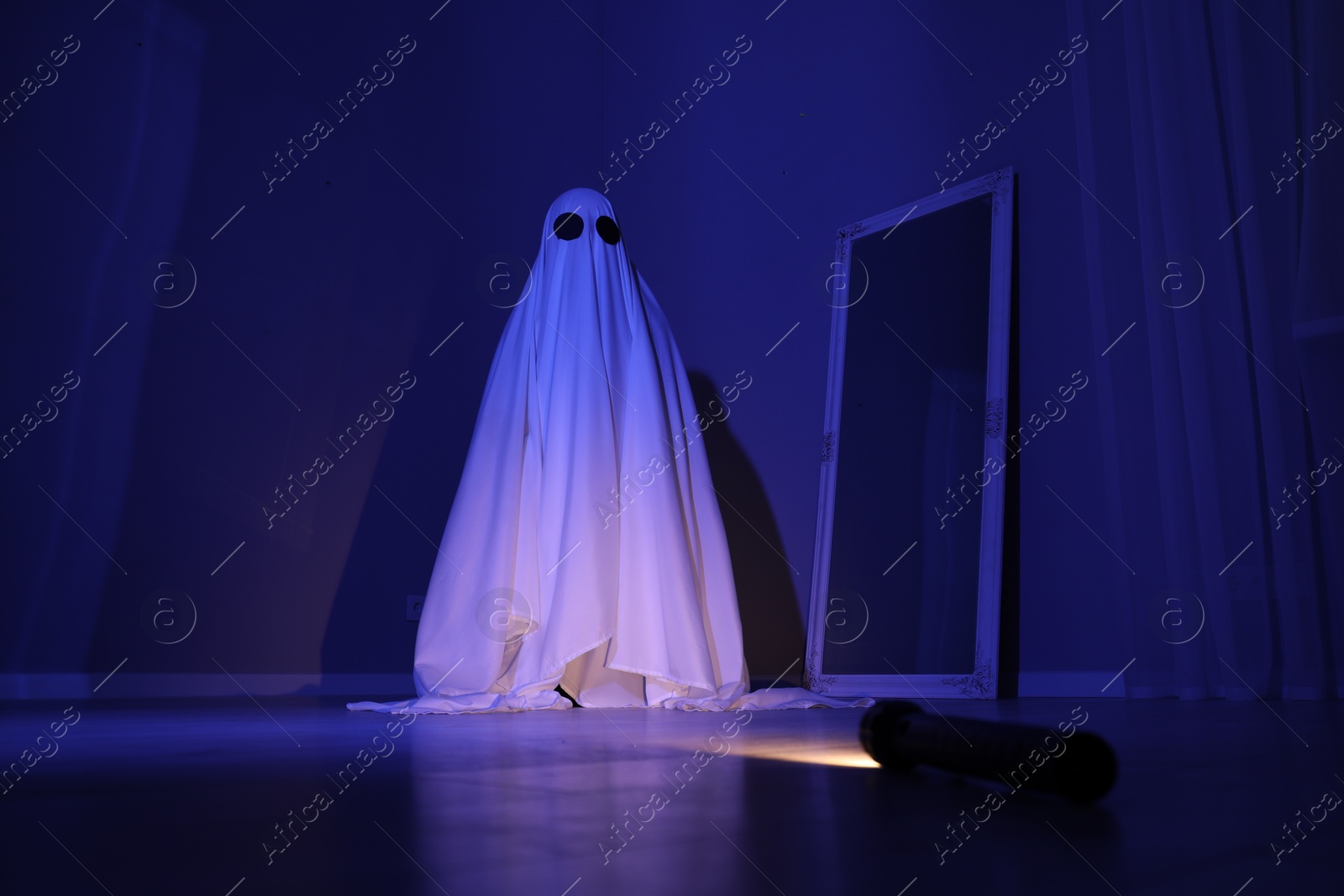 Photo of Creepy ghost. Woman covered with sheet in blue light, low angle view