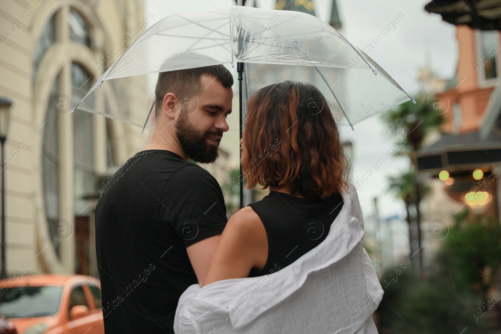 Photo of Young couple with umbrella enjoying time together under rain on city street