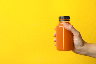Photo of Woman holding bottle of carrot juice on color background, closeup with space for text