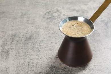 Photo of Turkish coffee pot with hot drink on grey table, space for text