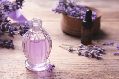 Glass bottle of natural cosmetic oil and lavender flowers on wooden table, space for text