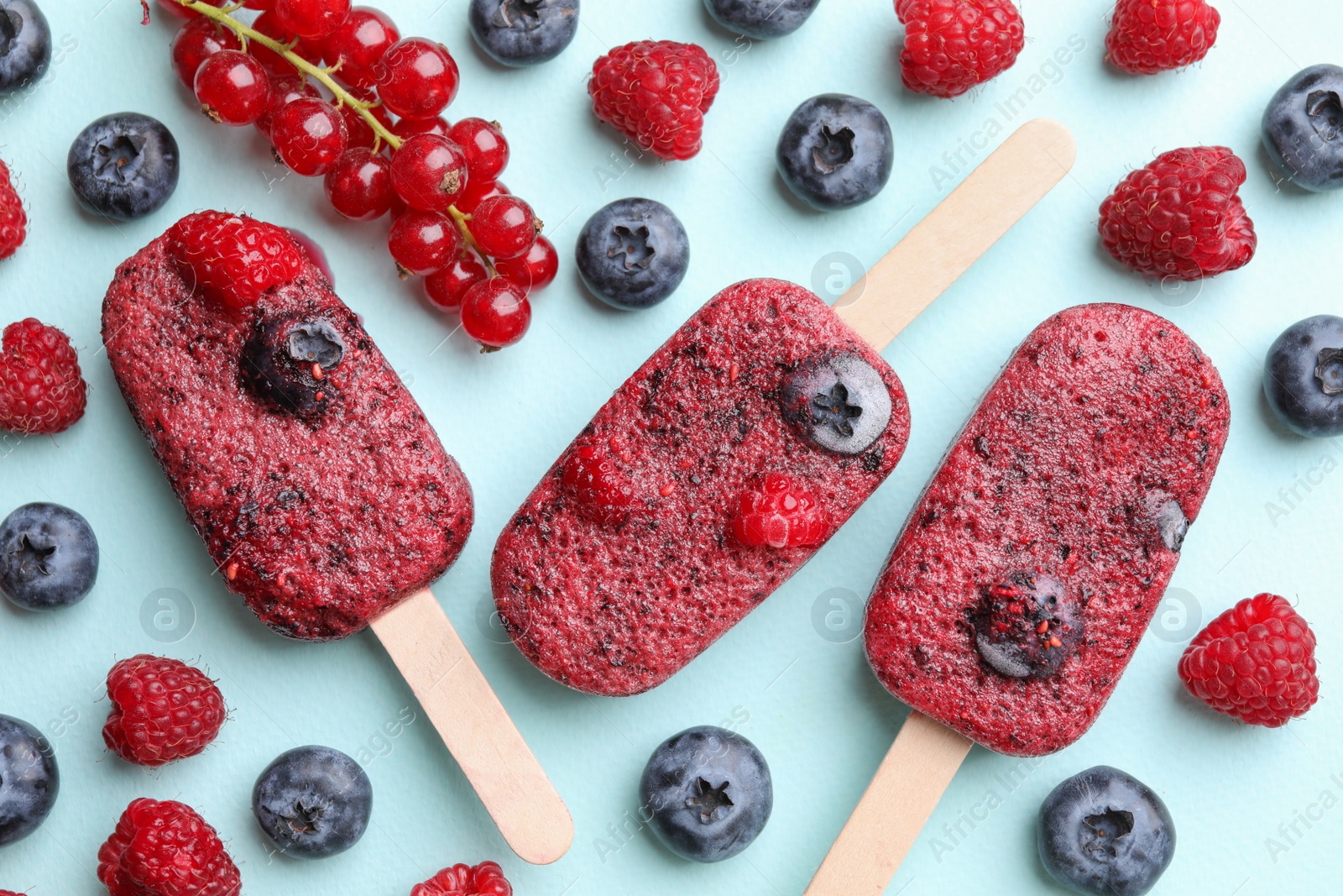 Photo of Tasty berry ice pops on light blue background, flat lay. Fruit popsicle