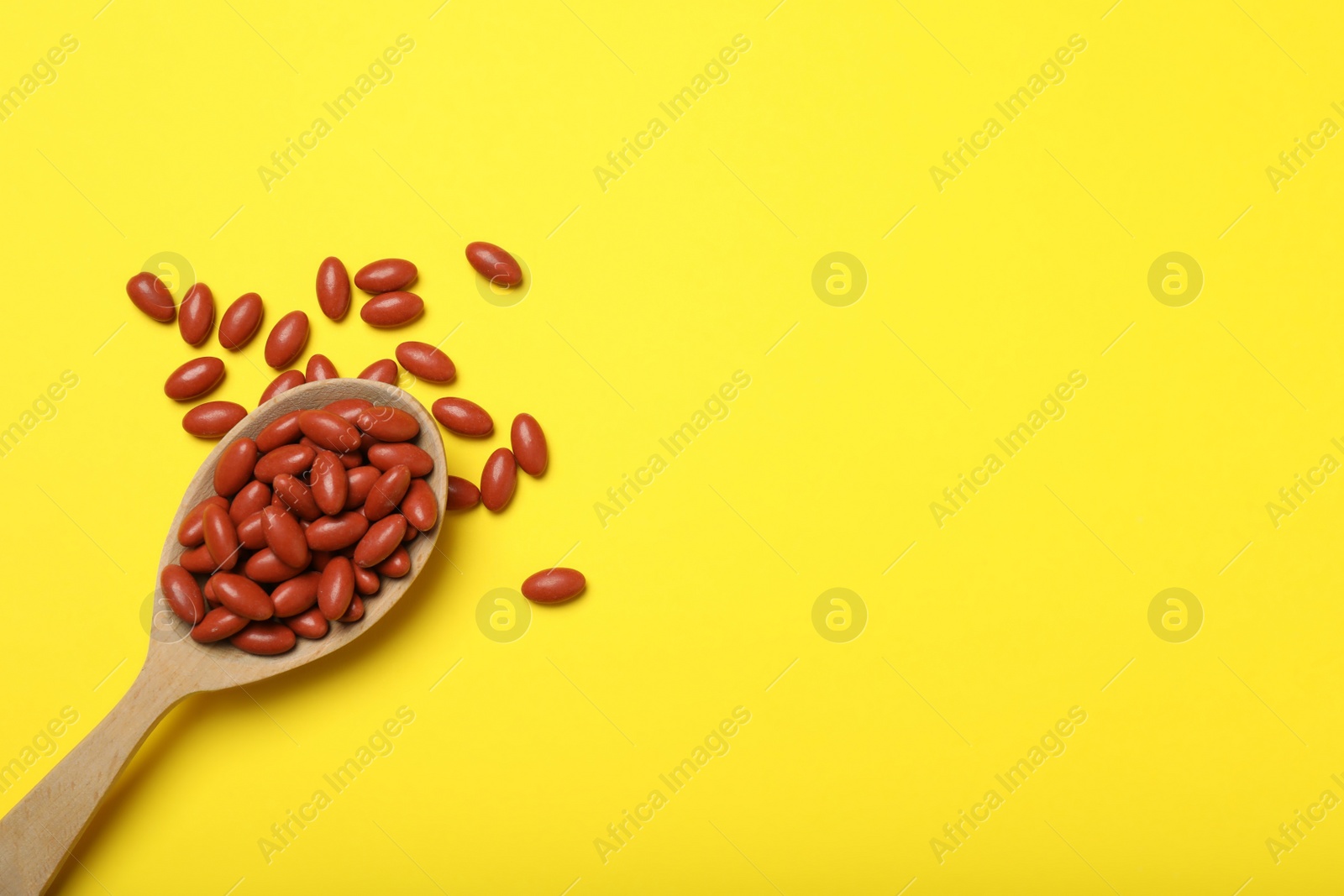 Photo of Wooden spoon with pills on yellow background, flat lay. Space for text