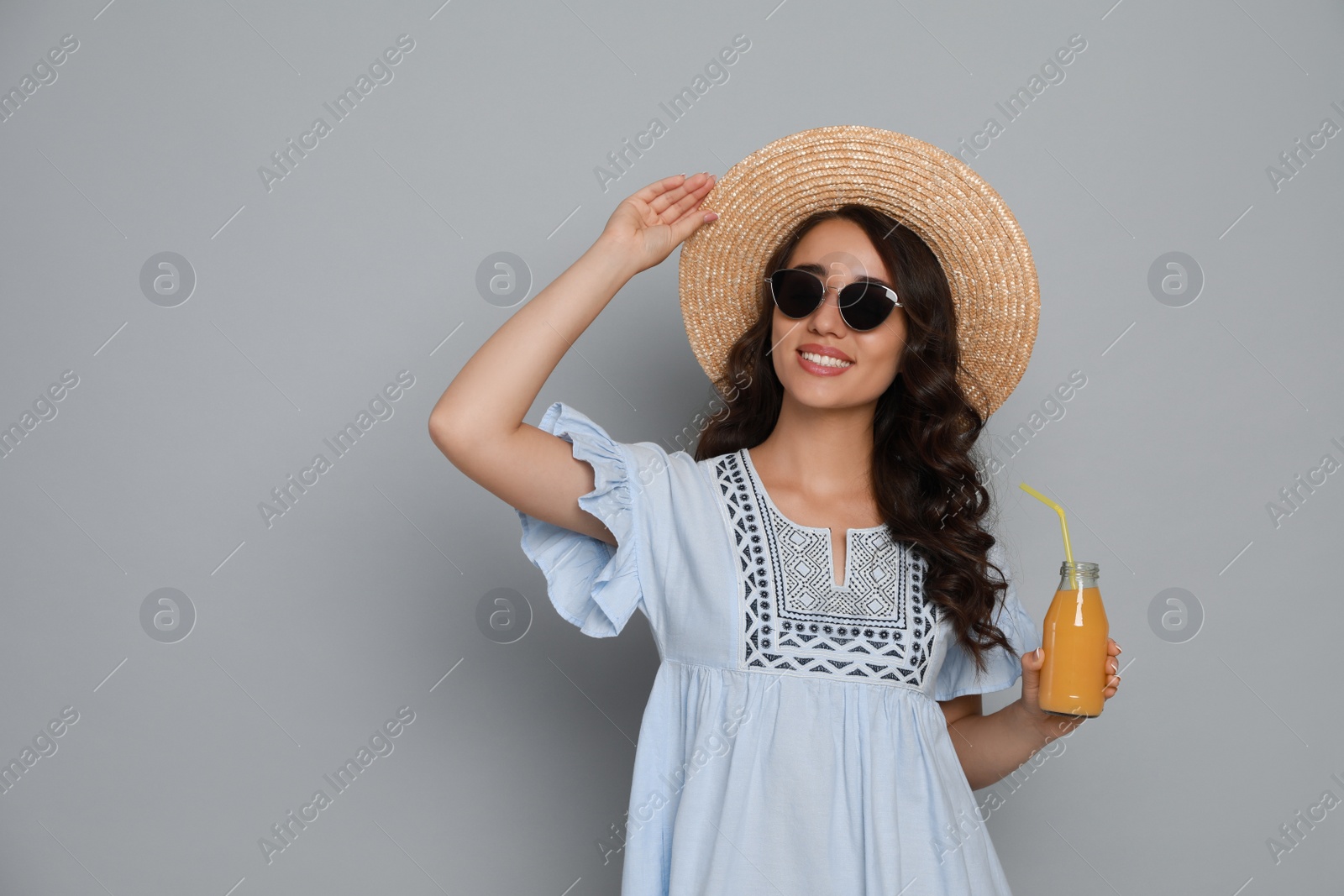 Photo of Beautiful young woman with straw hat and bottle of refreshing drink on light grey background. Space for text