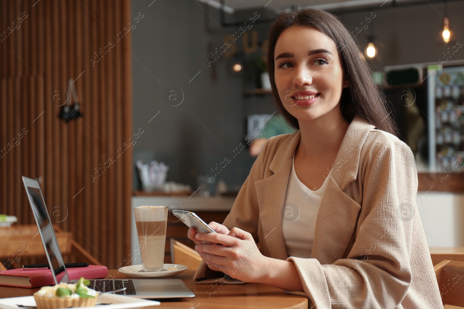 Photo of Young blogger with smartphone and laptop in cafe