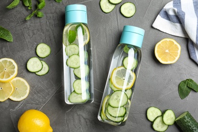 Bottles of refreshing water with cucumber, lemon and mint on black table, flat lay