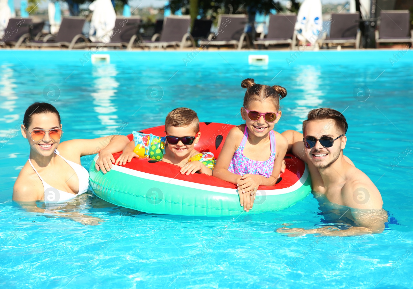 Photo of Young family with little children in swimming pool on sunny day