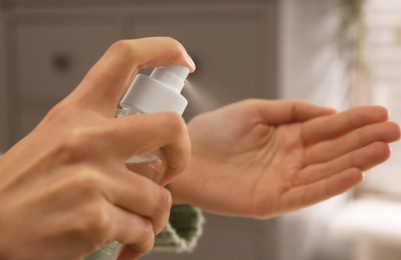 Photo of Young woman applying antiseptic spray indoors, closeup