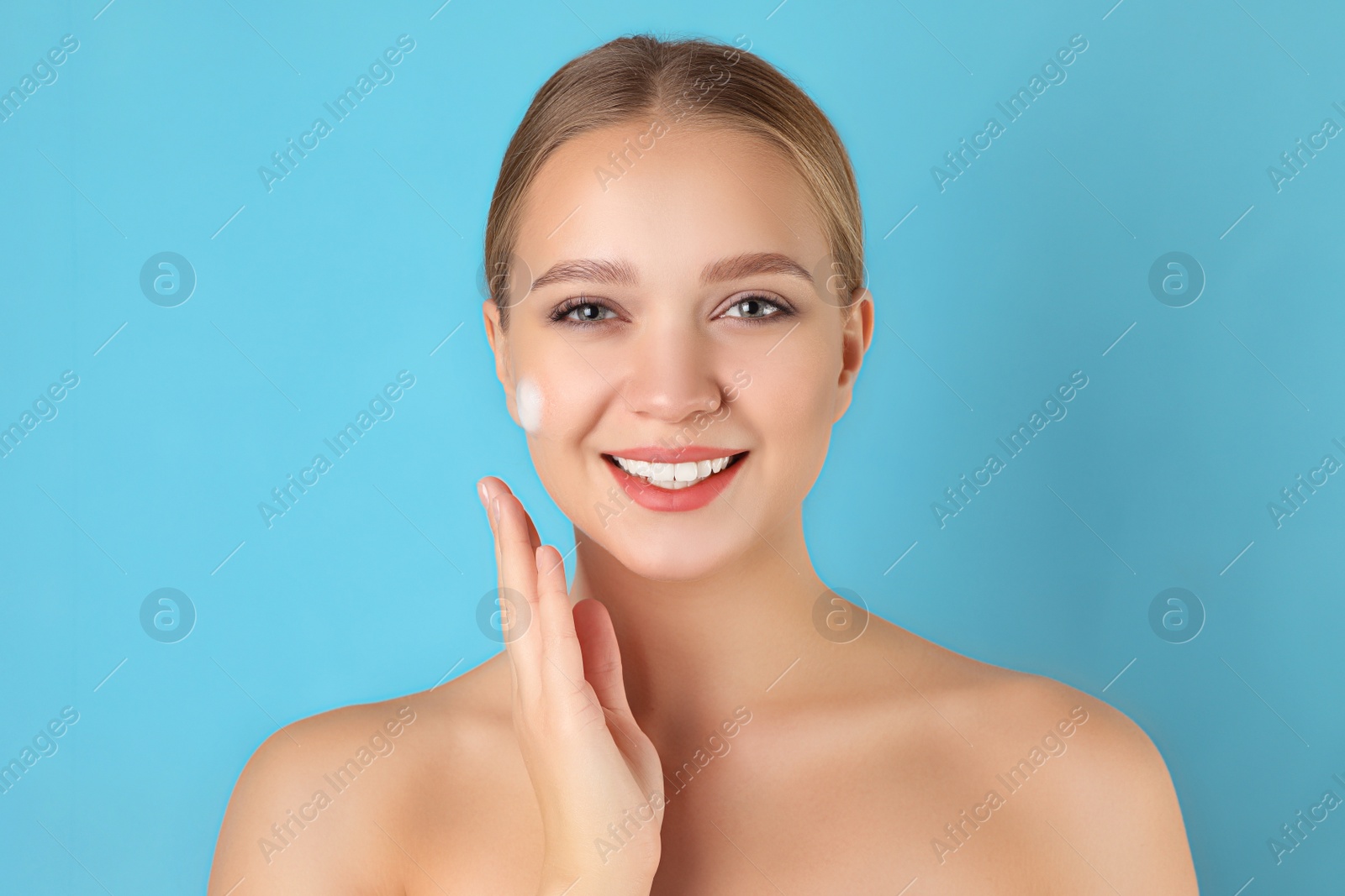 Photo of Young woman washing face with cleansing foam on light blue background. Cosmetic product