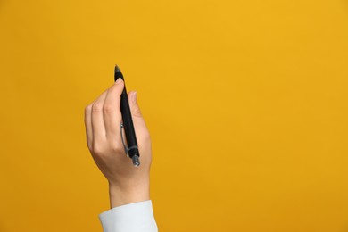Photo of Left-handed woman holding pen on yellow background, closeup. Space for text