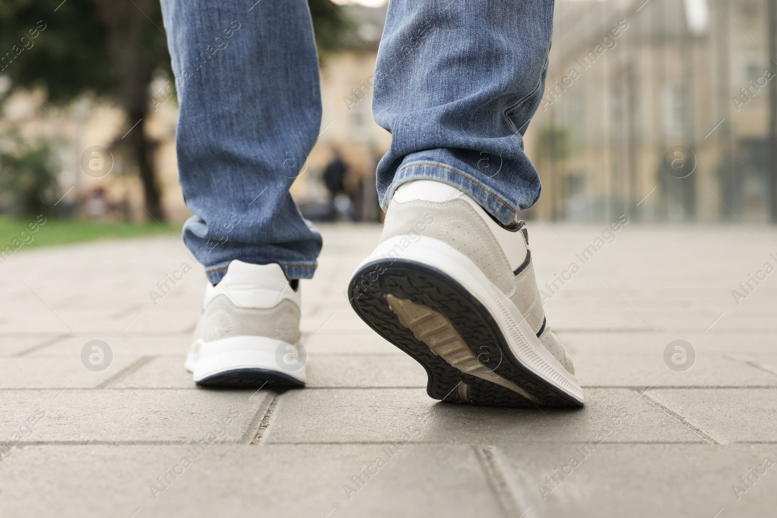 Photo of Man in jeans and sneakers walking on city street, closeup