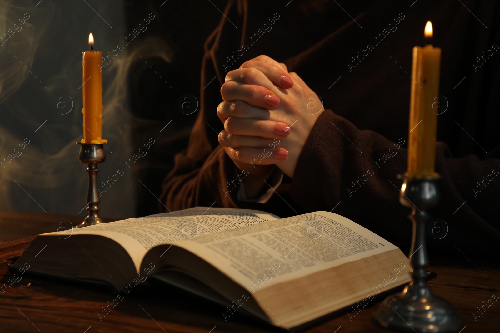 Photo of Woman praying at table with burning candles and Bible, closeup