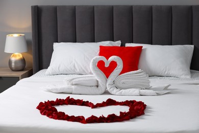 Photo of Honeymoon. Swans made with towels and heart of beautiful rose petals on bed in room