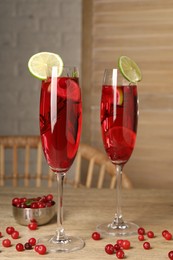 Tasty cranberry cocktail with rosemary and lime in glasses on wooden table
