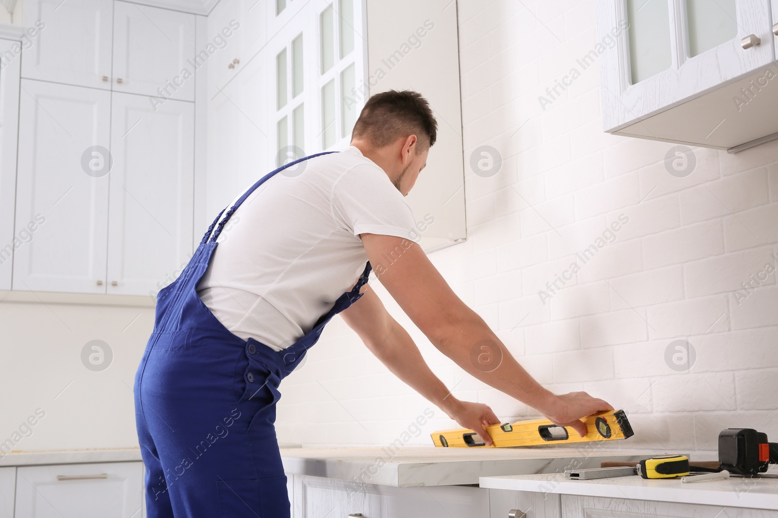 Photo of Worker measuring countertop with spirit level in kitchen