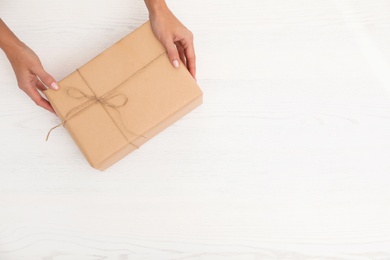 Photo of Woman holding parcel and space for text on wooden background, top view