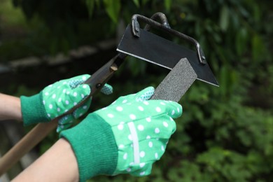 Photo of Woman sharpening hoe outdoors, closeup. Gardening tools