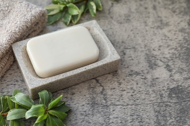 Photo of Dish with soap bar, terry towel and green plants on light grey textured table. Space for text