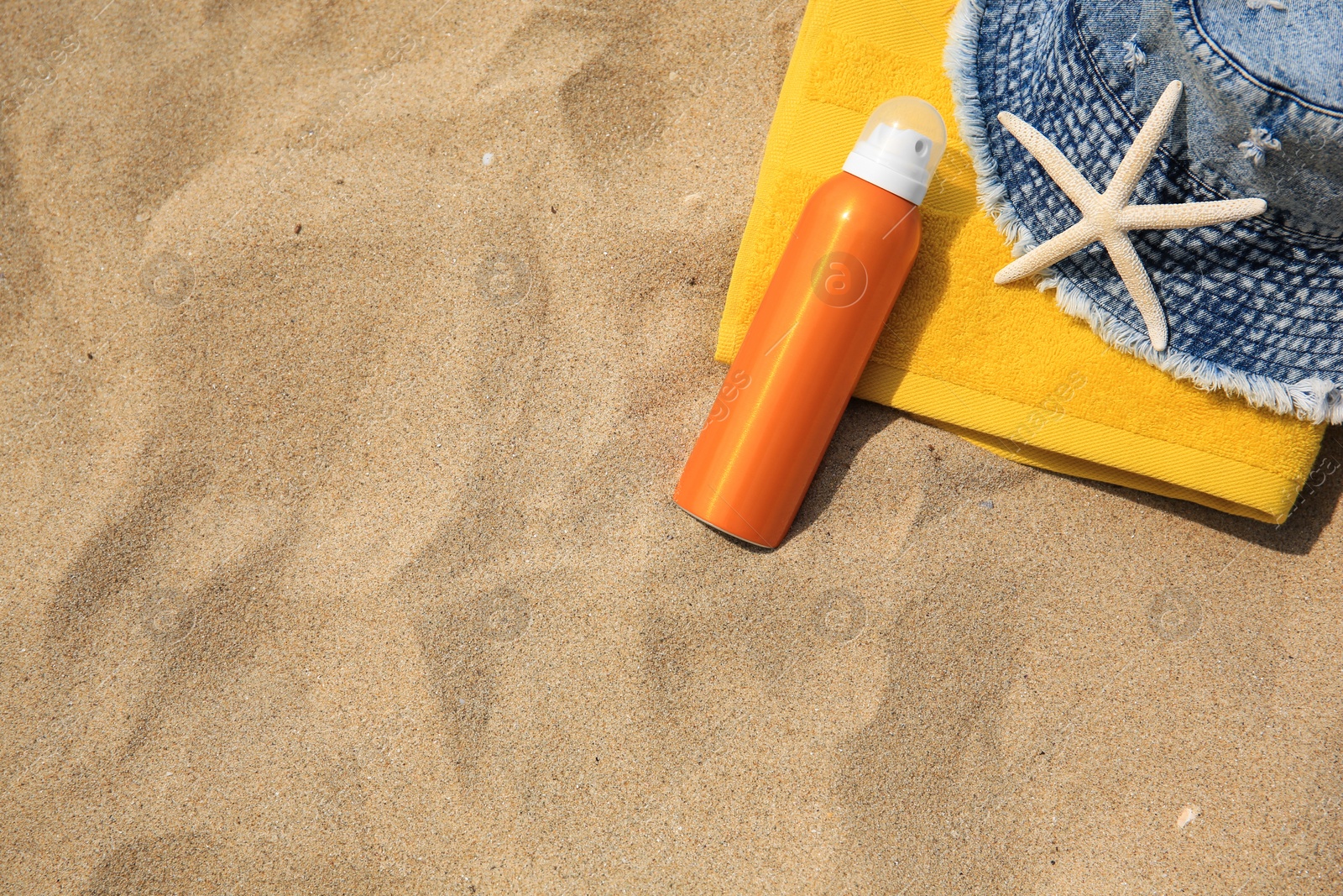 Photo of Sunscreen, panama hat, starfish and towel on sandy beach, top view and space for text. Sun protection