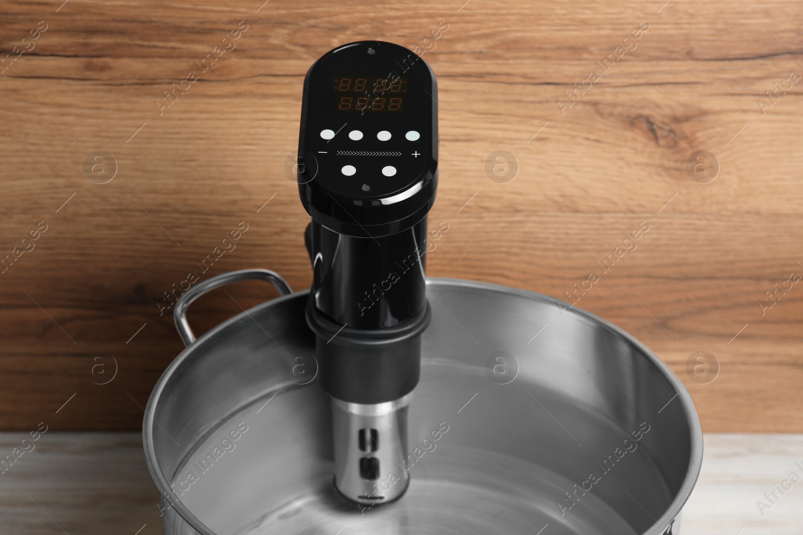 Photo of Sous vide cooker in pot on white wooden table. Thermal immersion circulator