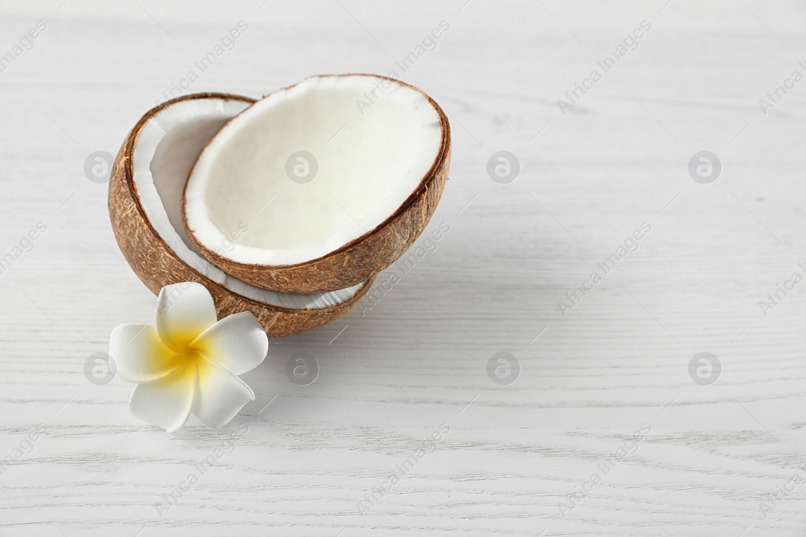 Photo of Halves of coconut and flower on white wooden background. Space for text