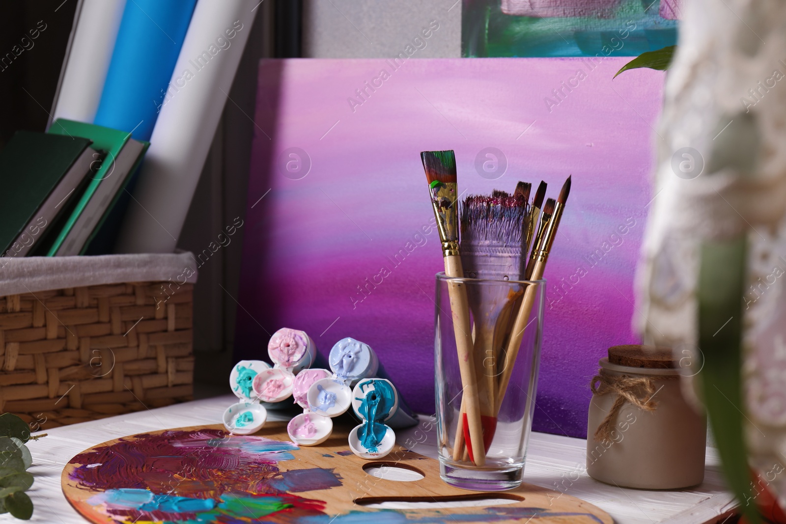 Photo of Wooden artist's palette with colorful paints, brushes and scented candle on white table