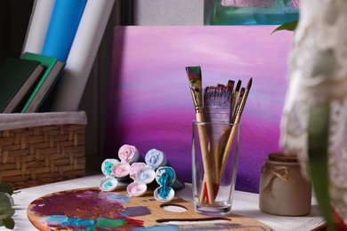 Wooden artist's palette with colorful paints, brushes and scented candle on white table