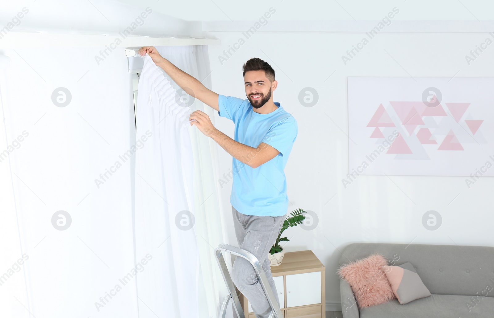 Photo of Young man hanging window curtain in room. Space for text