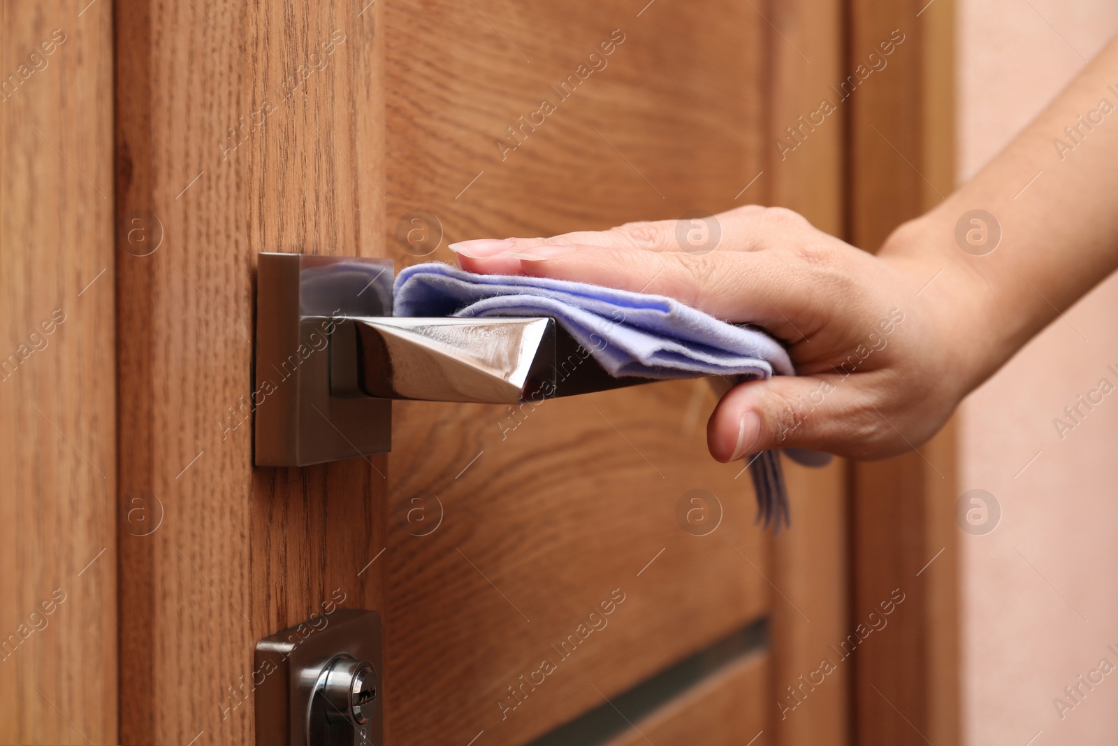 Photo of Woman cleaning door handle with rag indoors, closeup