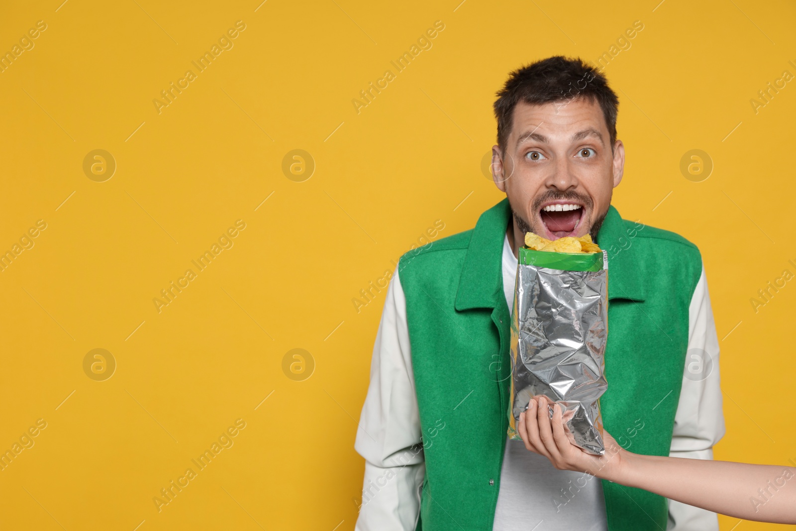 Photo of Woman offering tasty potato chips to excited man on orange background, space for text