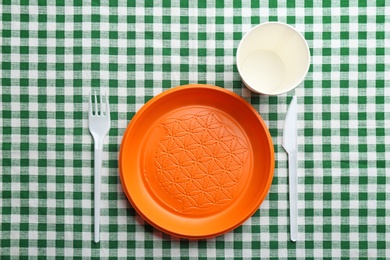 Photo of Composition with plastic dishware on checkered tablecloth, top view. Picnic table setting