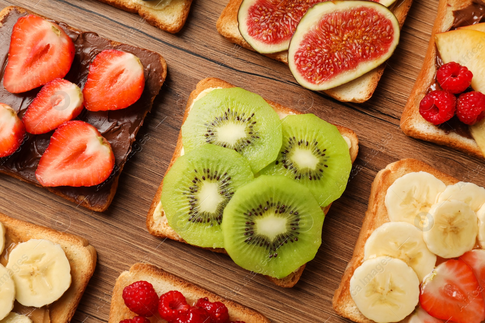 Photo of Tasty toasts with different spreads and fruits on wooden table, flat lay