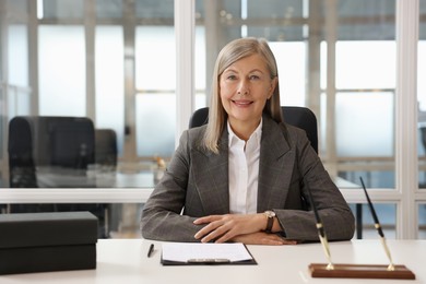 Photo of Smiling woman at table in office. Lawyer, businesswoman, accountant or manager