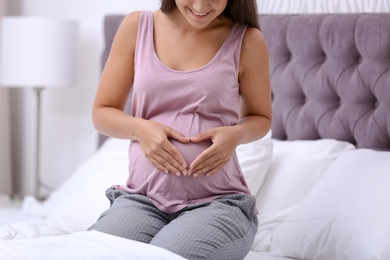 Happy pregnant woman sitting on bed at home, closeup